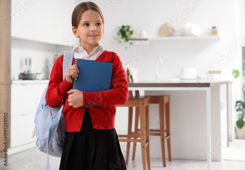 Cute schoolgirl with notebook and backpack in kitchen