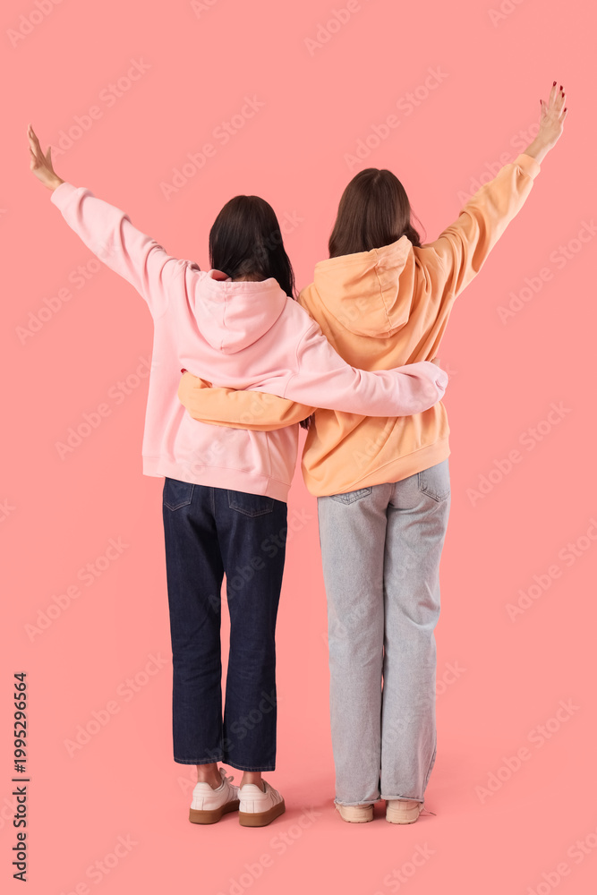 Fototapeta premium Teenage girls hugging on pink background, back view