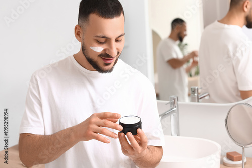 Young man applying cream on...