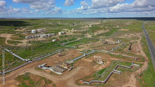 Aerial drone view processing hub with large storage tanks and dense pipeline grid, service roads and wellheads interlaced with green fields, industrial scale emphasized by textures, tanks