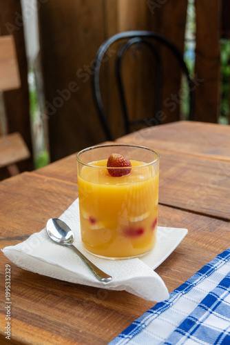 A vibrant orange-yellow layered fruit pudding with banana slices and a strawberry on top, presented on a rustic wooden table.
