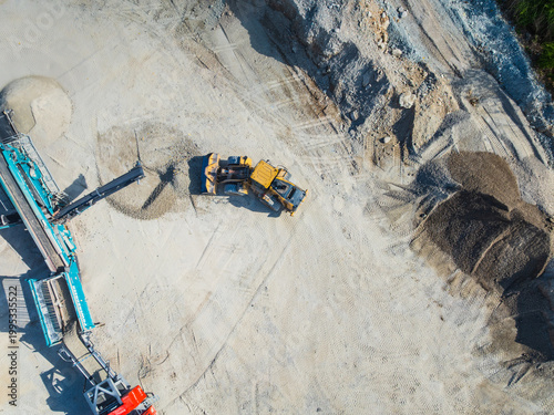 Aerial view of a yellow front loader moving gravel near a blue crushing machine at a construction site with piles of sand and dirt Indianapolis, Indiana, United States.