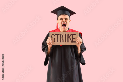 Protesting male graduate holding placard with word STRIKE on pink background