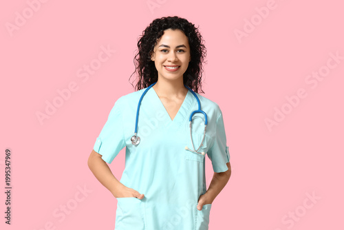 Beautiful young happy African-American female doctor with stethoscope on pink...