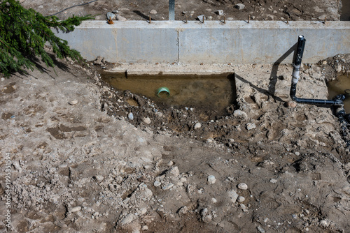 View from above of dirt foundation of new home build with standing rain water at low point with underground pipe installed, construction job site
