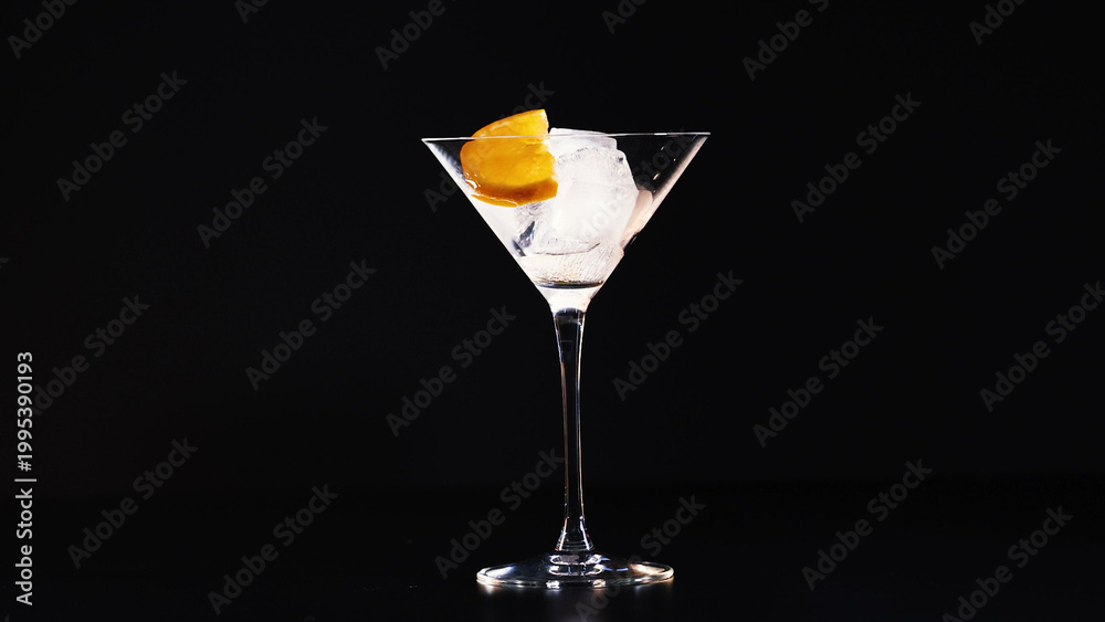 Fototapeta premium Empty cocktail glass filled with ice and orange garnish against black