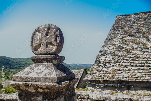 Occitan cross stone sculpture and traditional limestone roofs in Beynac