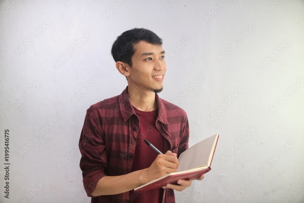 Naklejka premium Adult Asian man smiling friendly while writing in a note book