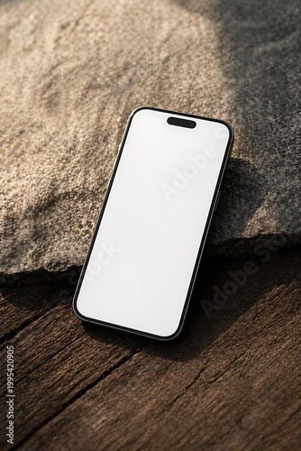A modern smartphone with a blank white screen rests on a textured wooden surface next to a large, rough stone.