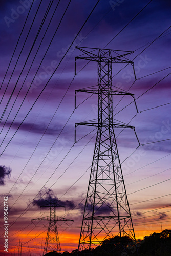 Foto High voltage power lines and transmission towers silhouetted against a dramatic sunset sky