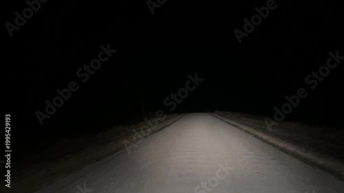 Vehicle headlights illuminating unpaved dirt road during nighttime rural travel