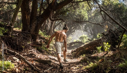 Shirtless man hiking on a sun-dappled forest trail surrounded by lush foliage and trees