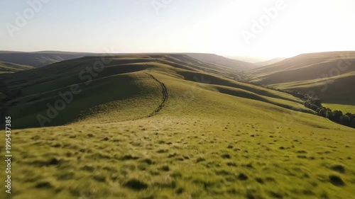 Rolling green hills under a bright sky with a path.