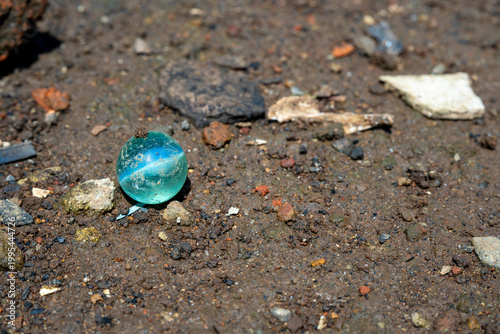 Round clear blue glass marble resting on rough dirt and pebbles