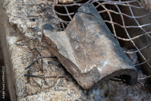 Broken charred clay fragment resting on a rusty metal wire grate