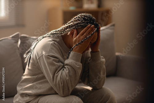 Quadro su tela Young woman sitting with head in hands on sofa, expressing stress, isolation, house arrest, home confinement concept