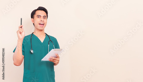 Photography Excited Southeast Asian male nurse or doctor in green scrubs and stethoscope having a great idea or eureka momenton isolated background