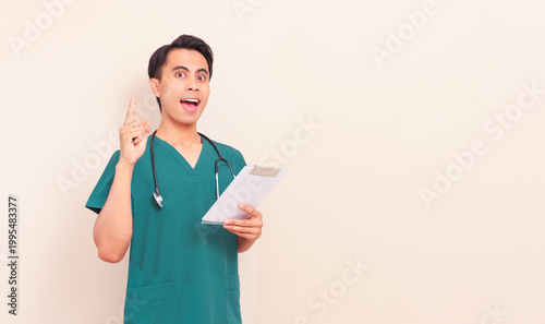 Foto Excited Southeast Asian male nurse or doctor in green scrubs and stethoscope having a great idea or eureka momenton isolated background