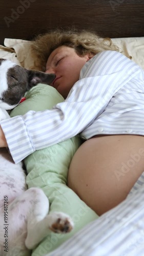 Tender moment of a pregnant woman with a bare belly sleeping soundly in bed, embracing her beloved dog and a pregnancy pillow, showcasing the serene bond between pet and owner