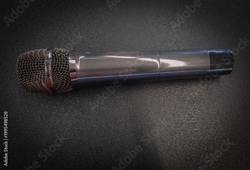 Professional handheld dynamic microphone placed on dark textured background with dramatic lighting Modern wireless microphone with steel mesh head on a textured black backdrop with soft light