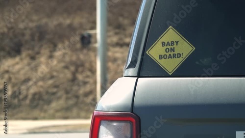Yellow Baby on Board sign on a car window in city traffic, emphasizing road safety for infants.