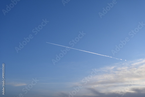 Fotografie A sleek jet soars across the boundless blue sky, leaving a crisp contrail that etches a temporary signature between cotton-like clouds