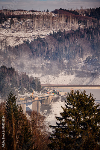 Close up of bridge construction site in snowy mountains with excavator and dead forest background