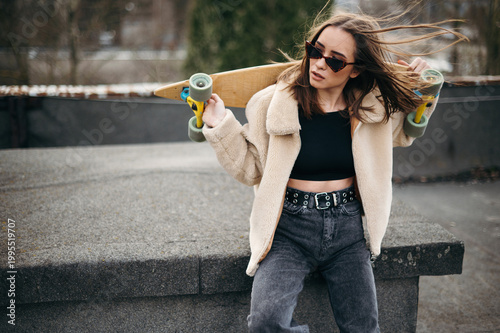 Young brunette in sunglasses posing on roof with skateboard