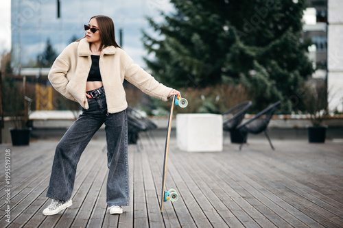 Woman in street clothes posing with skateboard in hands