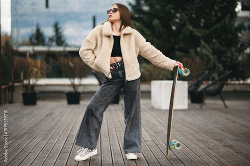 Woman in street clothes posing with skateboard in hands