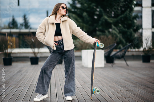 Woman in street clothes posing with skateboard in hands