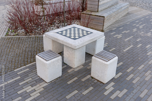 High angle view of concrete outdoor chess table and stools in modern city park. Square concrete game table with an integrated checkered board for chess or checkers, surrounded by three matching stools