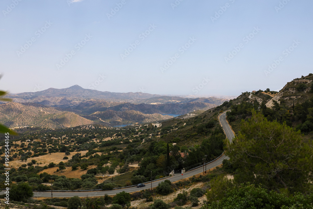 Obraz premium Scenic landscape of Pano Lefkara village area, Cyprus, with a winding mountain road and Mediterranean hills under a clear blue sky