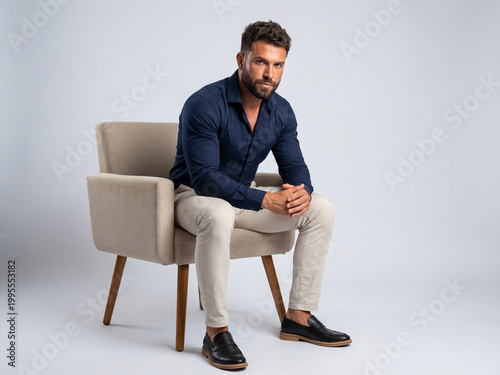 Studio portrait of a confident man sitting on a modern beige armchair