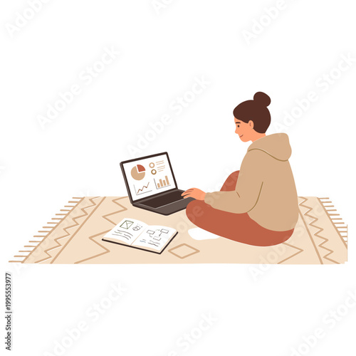 A woman sits cross-legged on a rug with a laptop and notebook indoors.