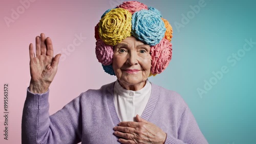 Elderly Woman with Colorful Flower Hat and Lavender Cardigan Poses with Hand Raised.