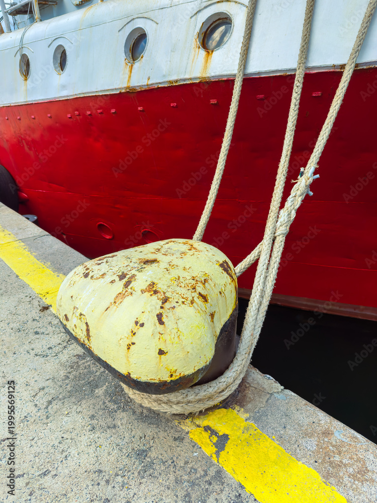 Fototapeta premium Rope tied to a yellow fender with a large ship in the background at the dock during daylight hours