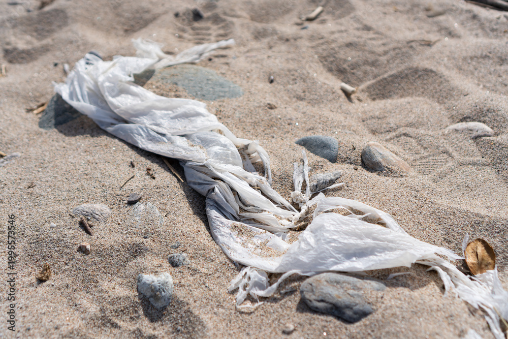 Obraz premium 砂浜に打ち上げられ埋もれかけた海洋プラスチックのビニールゴミ。美しい海岸を汚染する漂着ゴミが引き起こす深刻な環境問題。SDGsや海洋保護、プラスチック削減を啓発する、質感の際立つ横位置の自然環境素材。日本の海岸の現状を伝える風景。