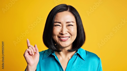 Surprised Asian Woman Covering Mouth with Hands on Yellow Background.