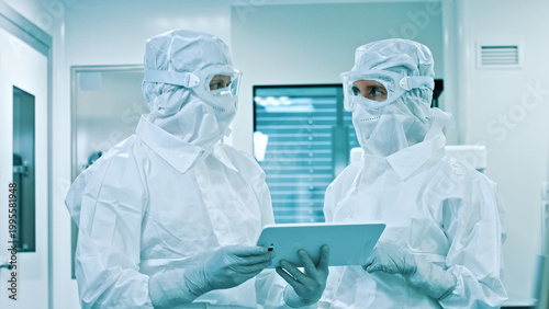 Fotografija Two researchers, dressed in clean suits, examine a tablet in a high-tech lab