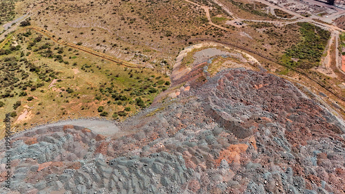 Aerial view of a vast, multi-hued mine dump, its textured grey and reddish strata contrasting with the arid, sparse land, Rustenburg, North West, South Africa.