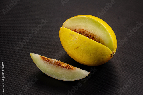 Fresh ripe yellow melon with a slice and visible seeds on a rustic background.