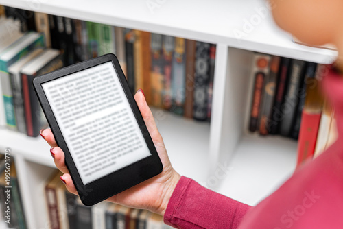 Slika na platnu A woman reads an e-reader near a bookcase