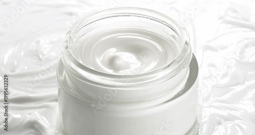 Open jar with cosmetic facial cream on a background of cream texture, close-up on a rotating table.