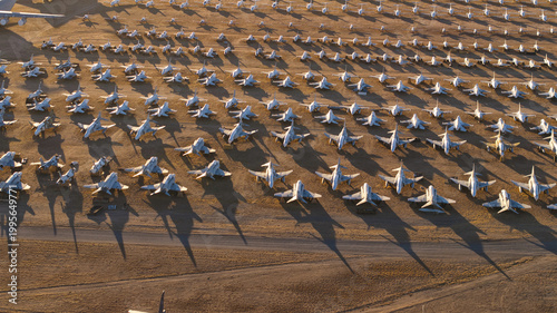 Tucson, United States - 06 February 2025: Aerial view of countless retired aircraft, stark white against the ochre desert, lined in silent, shadowed rows.