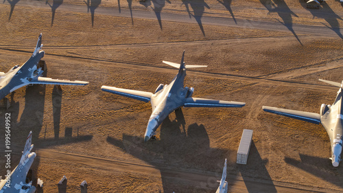 Tucson, United States - 06 February 2025: Aerial view of numerous grey warbirds resting on the vast, ochre desert floor, casting long, stark shadows under the golden light.