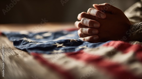 Close-up of praying hands resting on a folded national flag under warm natural light