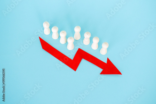 фотографія Line of wooden peg dolls stands behind red downward arrow on blue background