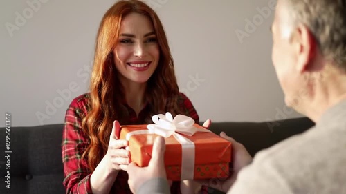 Smiling redhead woman covering eyes receiving surprise gift at home