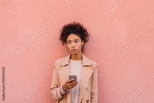 Confused young woman with smartphone against a pink wall